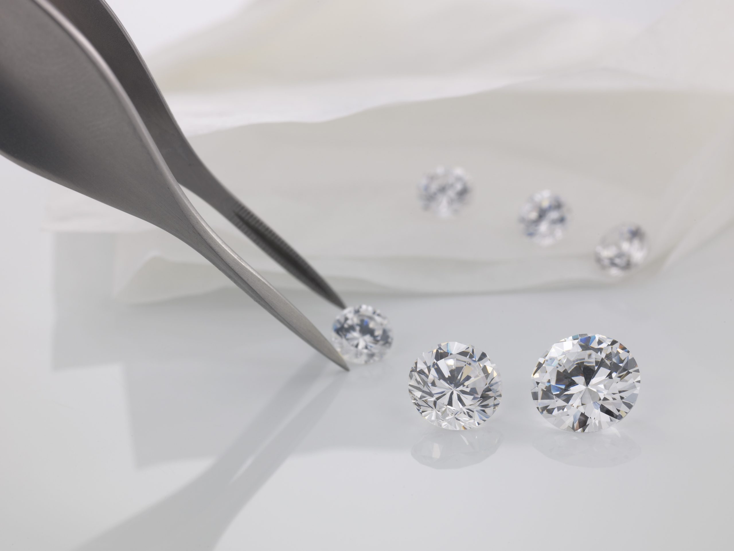 A gemologist selecting lab-grown diamonds with tweezers on a light background